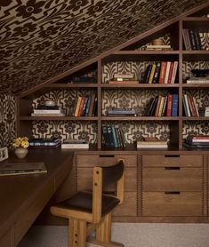 a room with a desk, bookshelf and chair in front of the wall