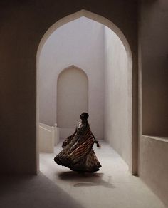 a woman in a long dress is walking through an arched hallway with white walls and arches