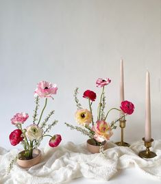 three small vases with flowers and candles on a white cloth next to each other