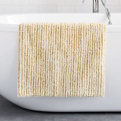 a yellow and white striped towel hanging on the side of a bathtub