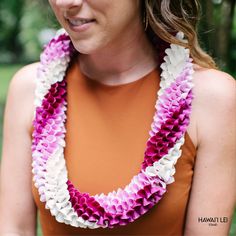 a woman in an orange top is wearing a purple and white flower lei around her neck