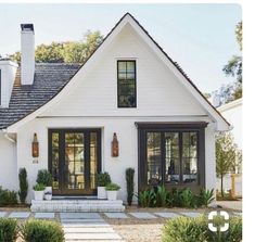 a white house with black shutters and windows on the front door is surrounded by greenery