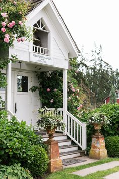 a small white house with pink flowers on the front porch and steps leading up to it