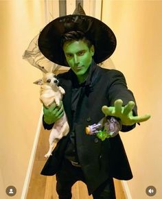 a man dressed in green holding a dog and wearing a witches hat with his hands