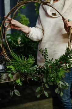 a woman holding a wreath made out of branches and greenery in front of her face