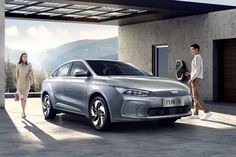 two people walking towards a silver car in front of a building with an open door