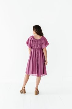 Features Round neckline Short puff sleeve with elastic cuff Elastic waist Smocked back Fully lined Pockets Deep orchid color with shimmer overlay Dress & Lining: 100% Polyester Size + Fit XS 00-2, Small 2-6, Medium 8-10, Large 12-14, X-Large 14-16, 2X 20-22, 3X 24-26, 4X 28-30 Kristin is 5'4", a size 1 and is wearing a Small Jaycie is 5'6", a size 18 and is wearing a 2X Runs true to size. Bust Measurements taken while laying flat and then doubled. They do no account for stretch. Click here for s Solid Flowy Smocked Dress For Spring, Solid Color Flowy Smocked Dress For Brunch, Flowy Solid Smocked Dress For Brunch, Billowy Solid Dress For Spring, Spring Solid Color Billowy Dress, Spring Billowy Solid Color Dress, Daywear Flutter Sleeve Midi Dress With Smocked Bodice, Flowy Smocked Dress With Gathered Neckline For Daywear, Chic Smocked Dress With Short Elastic Sleeves