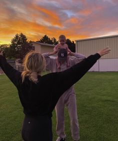 a woman holding a child in her arms while standing on top of a grass covered field