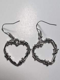 Barbed Wire Heart Earrings    Silver coloured heart shape charms with a look of barbed wire.  Silver coloured earring hooks.  24mm by 24mm by 2mm.  Brand new item in it's original packaging.  Check out the photos for a great view of the items.  Age 6+. Silver Grunge Jewelry For Valentine's Day, Grunge Style Heart-shaped Metal Jewelry, Punk Style Heart-shaped Metal Jewelry, Nickel-free Heart Earrings For Festivals, Nickel Free Heart Earrings For Festivals, Edgy Metal Jewelry With Heart Charm, Trendy Metal Heart Pierced Earrings, Emo Style Heart-shaped Metal Jewelry, Heart-shaped Metal Jewelry For Festival