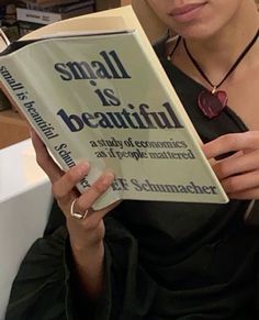 a woman is reading a book while wearing a necklace and holding it in her hands