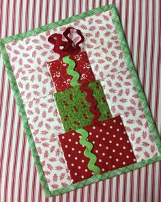 a red and green patchwork christmas tree ornament on a striped table cloth