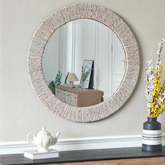 a mirror on the wall above a dresser with vases and flowers next to it