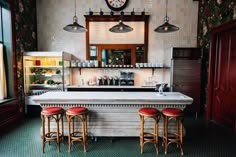 a bar with three stools in front of it and a clock on the wall