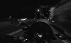 black and white photograph of motorcycle in motion on roadway at night time with headlights visible