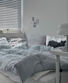 an unmade bed sitting next to a window in a room with white walls and windows