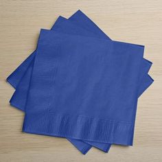 blue paper napkins stacked on top of each other in front of a wooden table