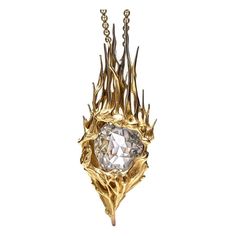 a gold necklace with a white diamond in the center and some branches hanging from it