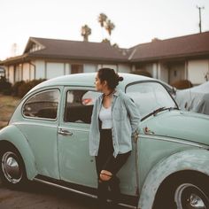 a woman leaning on the hood of an old green car in front of a house