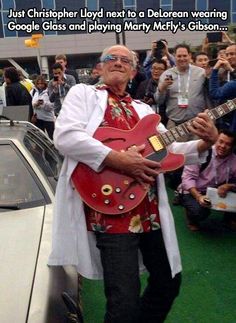 an older man holding a red guitar while standing next to a white car