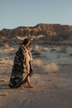 a woman wrapped in a blanket walking through the desert