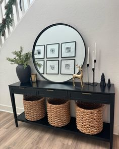 a black console table with baskets underneath it and a round mirror on the wall above