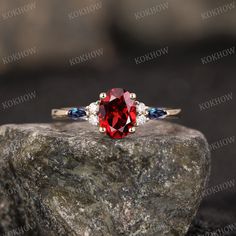 a red and blue stone ring sitting on top of a rock with two diamonds around it