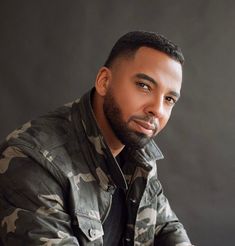 a man in camo jacket sitting down with his hands on his knees and looking at the camera