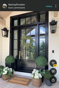 a black front door with two potted plants on the side and a welcome mat