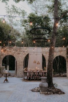 an outdoor dining area with lights strung from the ceiling and tables set up under trees