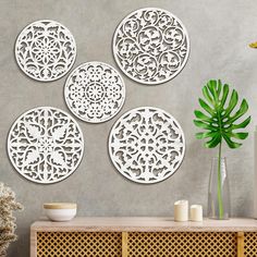 four circular metal wall art pieces on a grey wall next to a potted plant