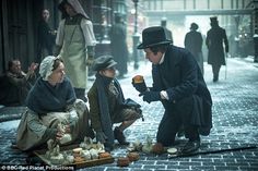 a man and woman sitting on the ground in front of an old fashioned street vendor