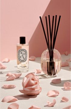 a bottle of reeds next to a vase filled with pink flowers and sticks on a table