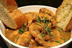 a white bowl filled with chicken and gravy next to a piece of bread