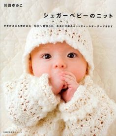 a baby wearing a white crochet jacket and hat with hands in her mouth