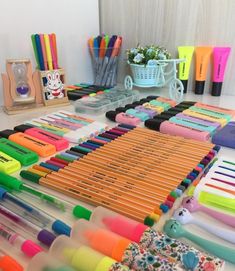 there are many different colored pens and pencils on the table with other office supplies