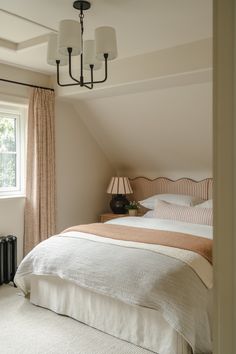 a bed sitting under a window in a bedroom next to a lamp on a table