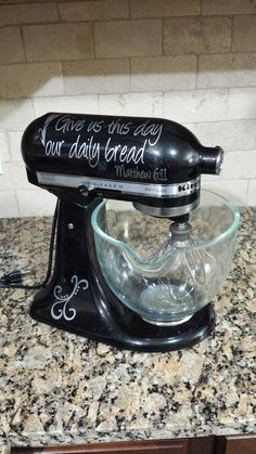 a black mixer sitting on top of a kitchen counter next to a brick wall with writing on it