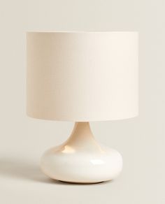 a white table lamp with a cream shade on it's base, against a plain background