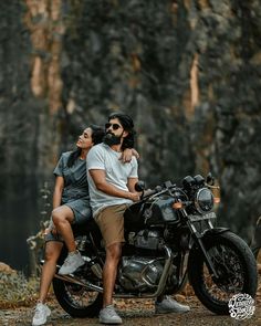 a man and woman sitting on a motorcycle in front of some trees with their heads turned to the side