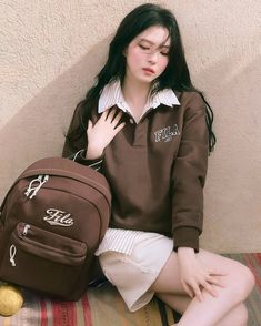 a woman sitting on the ground with a brown backpack in front of her, wearing white shorts and a polo shirt