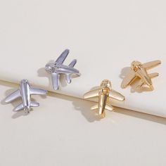 three pairs of gold and silver airplane studs on top of a white surface,