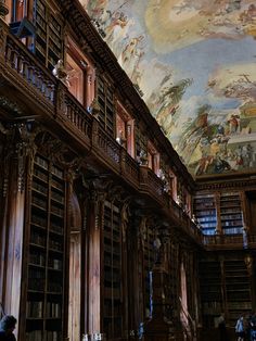 people are standing in the middle of a large room with bookshelves and paintings on the ceiling