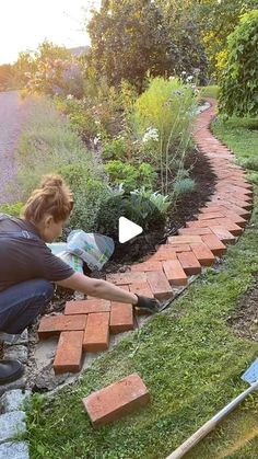 a woman kneeling down next to a brick path in the grass with flowers growing on it