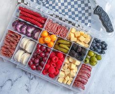 a plastic container filled with assorted fruits and veggies next to a knife