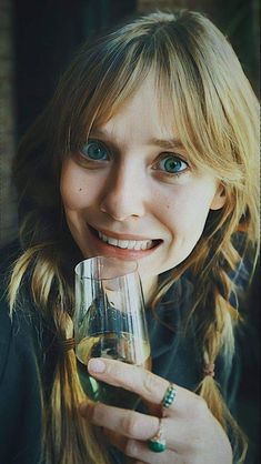 a woman holding a wine glass in her right hand and smiling at the camera with blue eyes