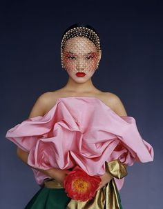 a woman in a pink top and green skirt with gold accents on her face, holding a red flower