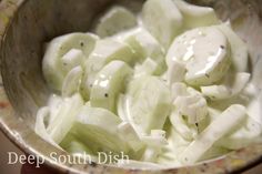 a metal bowl filled with cucumbers covered in white sauce on top of a table