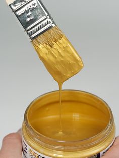 a person is holding a paintbrush over a jar of yellow food coloring liquid that has been poured onto it