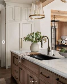 a kitchen with wooden cabinets and marble counter tops, hanging lights over the sink area