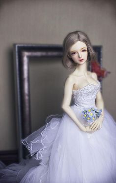 a doll is dressed in a white dress and holding a blue flower on her wedding day